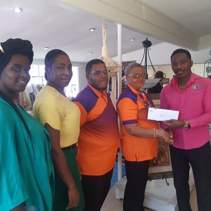 Hon. Adrian Forde, M.P, presenting a cheque to Ms. Janette Lynton with 4 people looking on