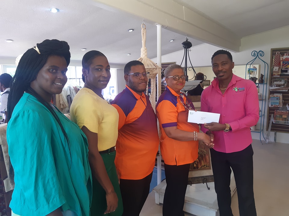 Hon. Adrian Forde, M.P, presenting a cheque to Ms. Janette Lynton with 4 people looking on